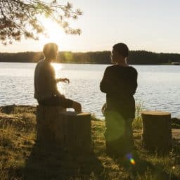 Two people talking outside while sitting next to a lake.
