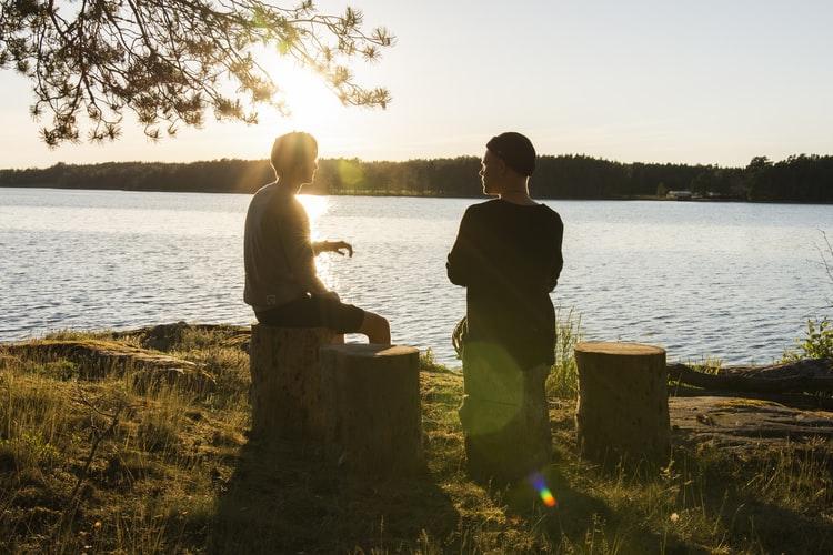 Two people talking outside while sitting next to a lake.