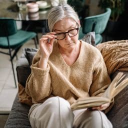 Older woman with glasses reading at home.