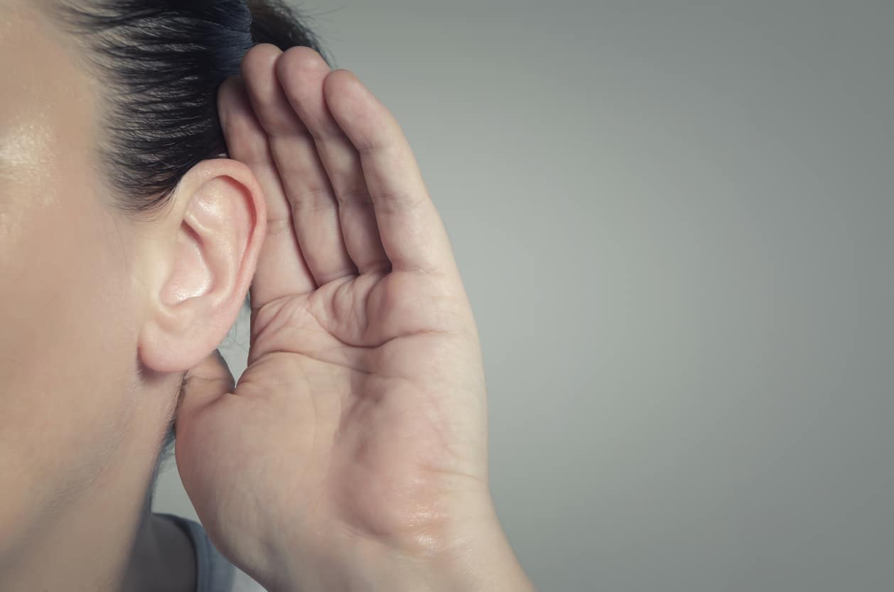 Close-up of a woman cupping her ear with her hand to try and hear better.