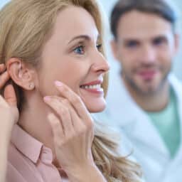 Woman adjusts hearing aids behind ear