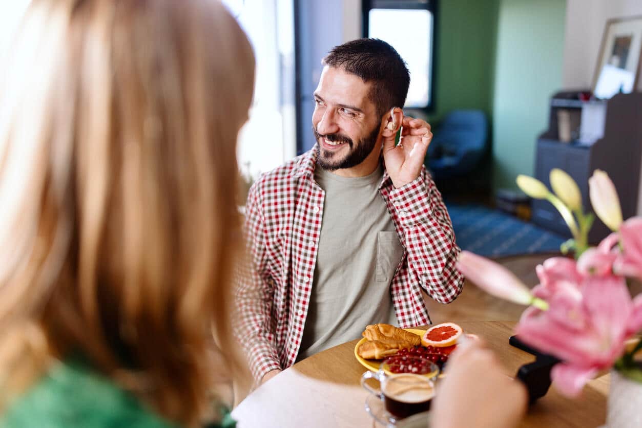 Happy man wearing hearing aids at breakfast.