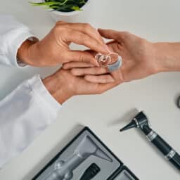 Audiologist hands the patient their new hearing aids over a table with hearing instruments.